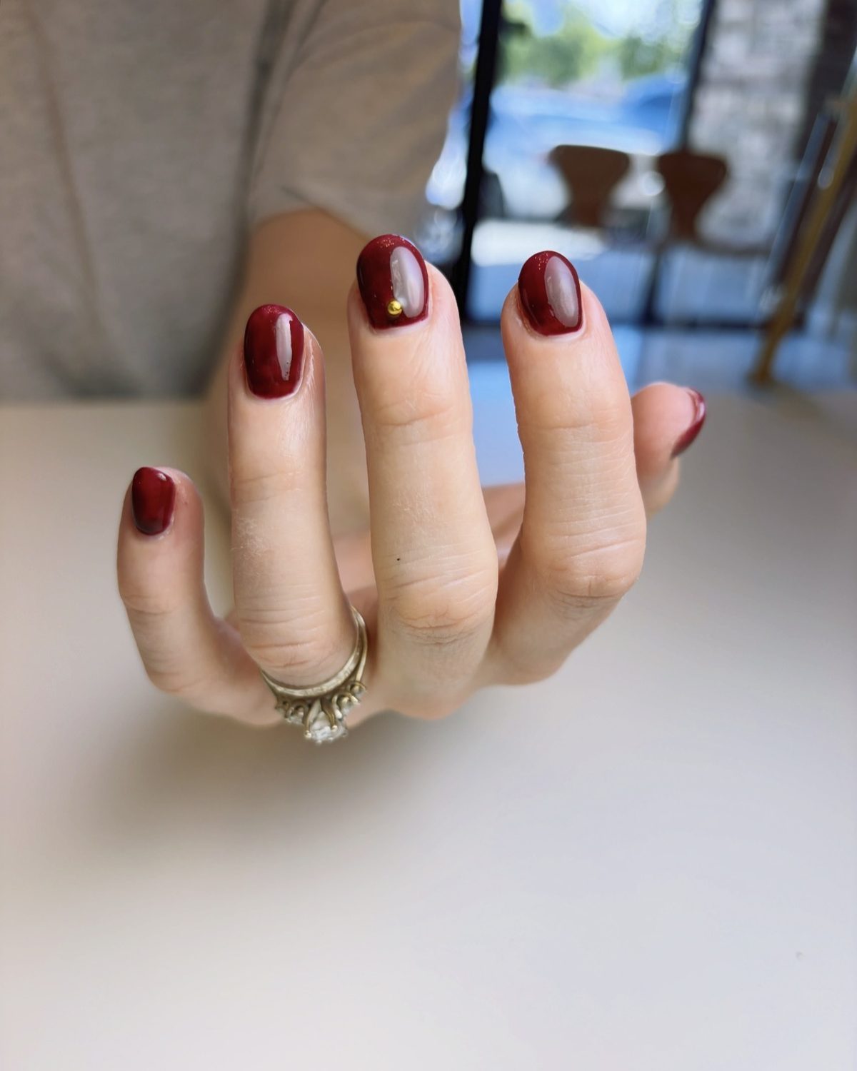 Short oval nails in a glossy cherry red with a tiny gold stud.